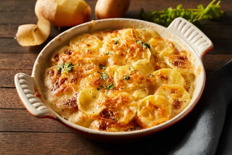 Scalloped gratin potatoes topped with grated cheese and herbs in a ceramic baking dish